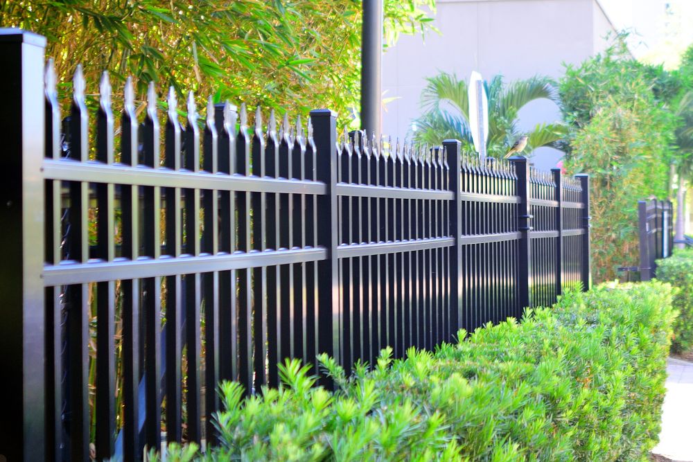 A black fence stands alongside a concrete sidewalk, creating a clear boundary between the two.