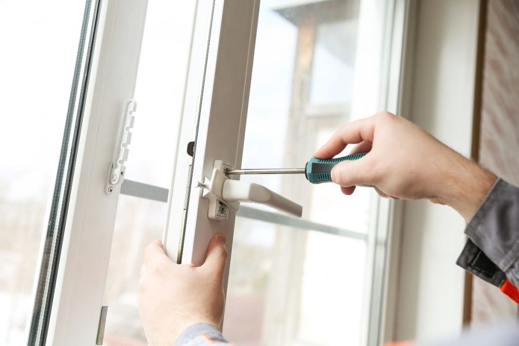 A man is using a screwdriver to fix a window, demonstrating home maintenance skills in a well-lit environment.